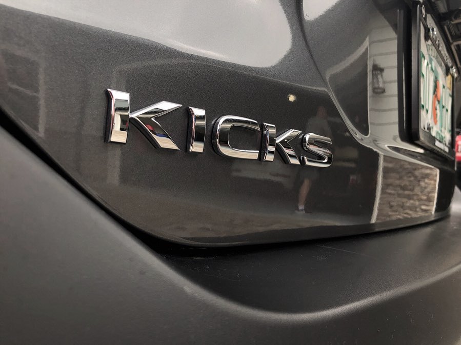 A close-up of the chrome Kicks lettering on the rear hatch of the gray Nissan.