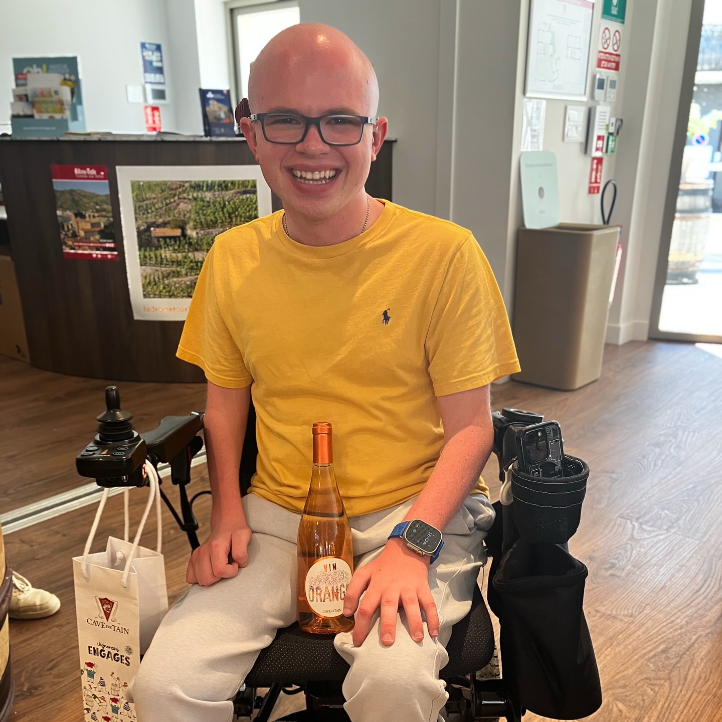 Ryleigh Newman in his wheelchair holding a bottle of orange wine given to him as a birthday gift in the Cave de Tain tasting room.