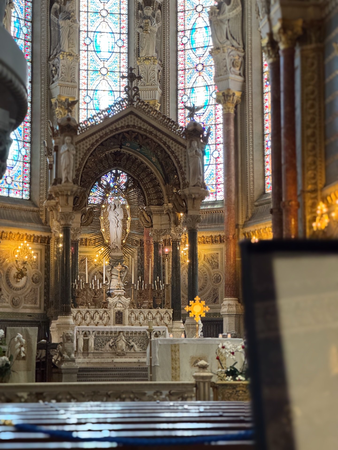 The gilded high altar of the Fourviere basilica glowing beneath tall stained glass windows in Lyon.